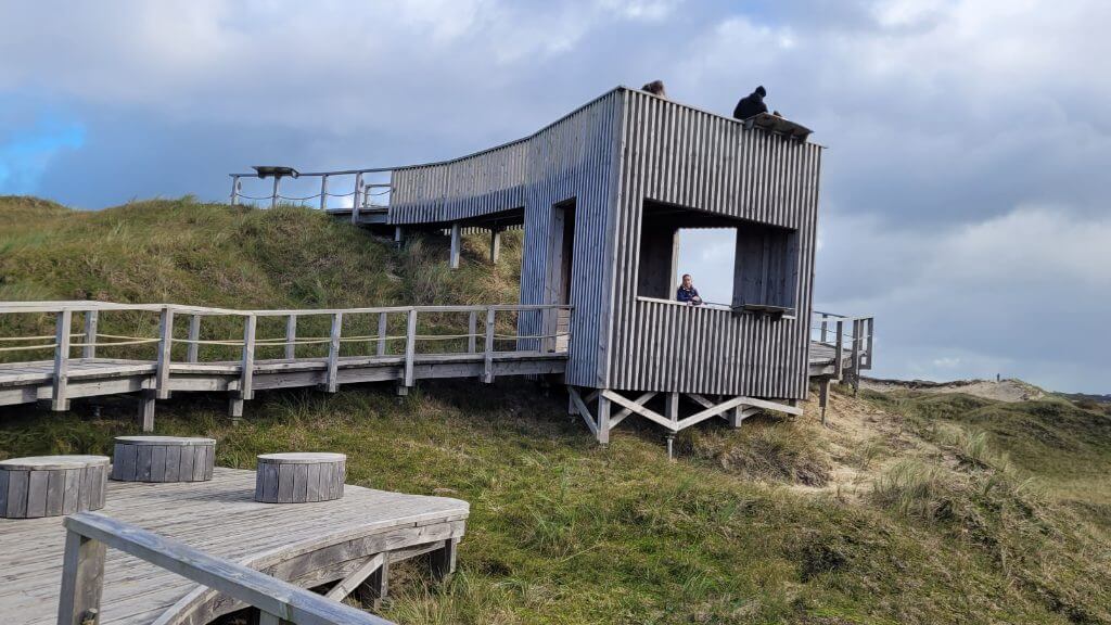 Moderner Aussichtsturm mit Sitzplätzen auf den Dünen unter bewölktem Himmel