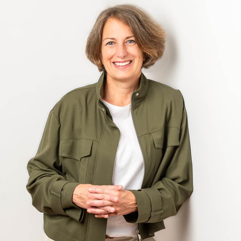 Frau in grüner Jacke lächelt vor weißem Hintergrund