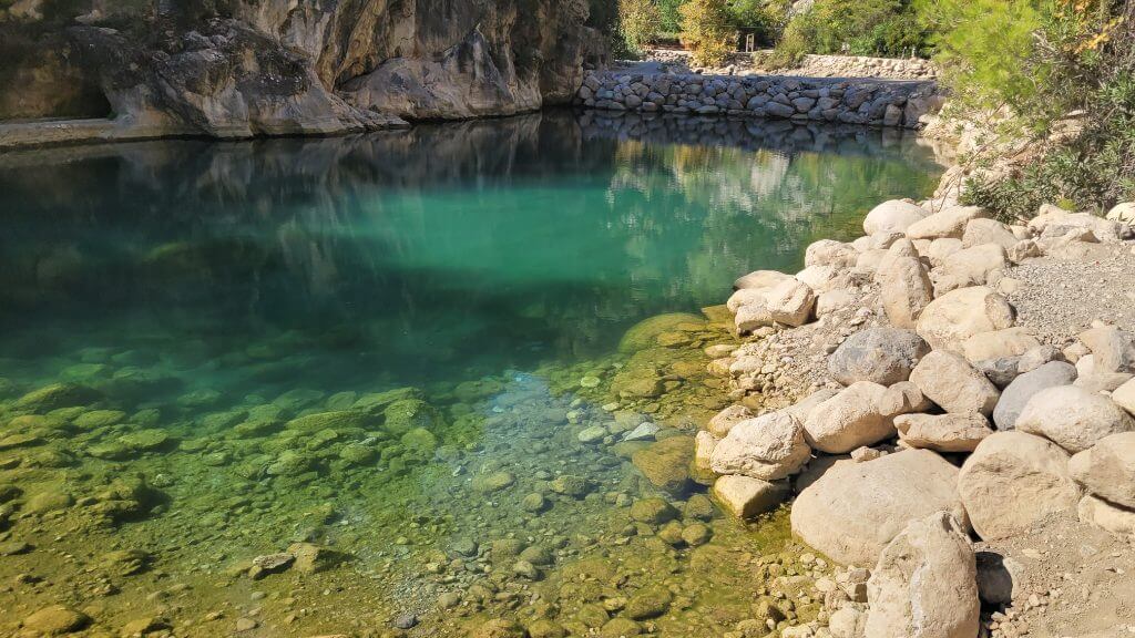 Nahaufnahme eines klaren Bergsees mit grünem Wasser und Steinen am Ufer.