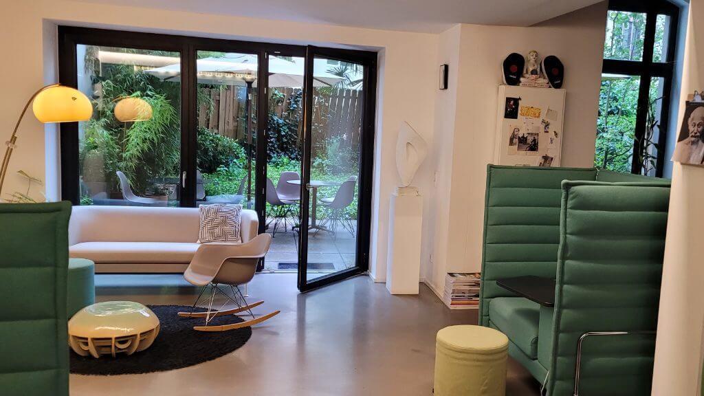 Heller Loungebereich mit Sofa, Schaukelstuhl und Zugang zu einem grünen Garten durch große Glasfenster.