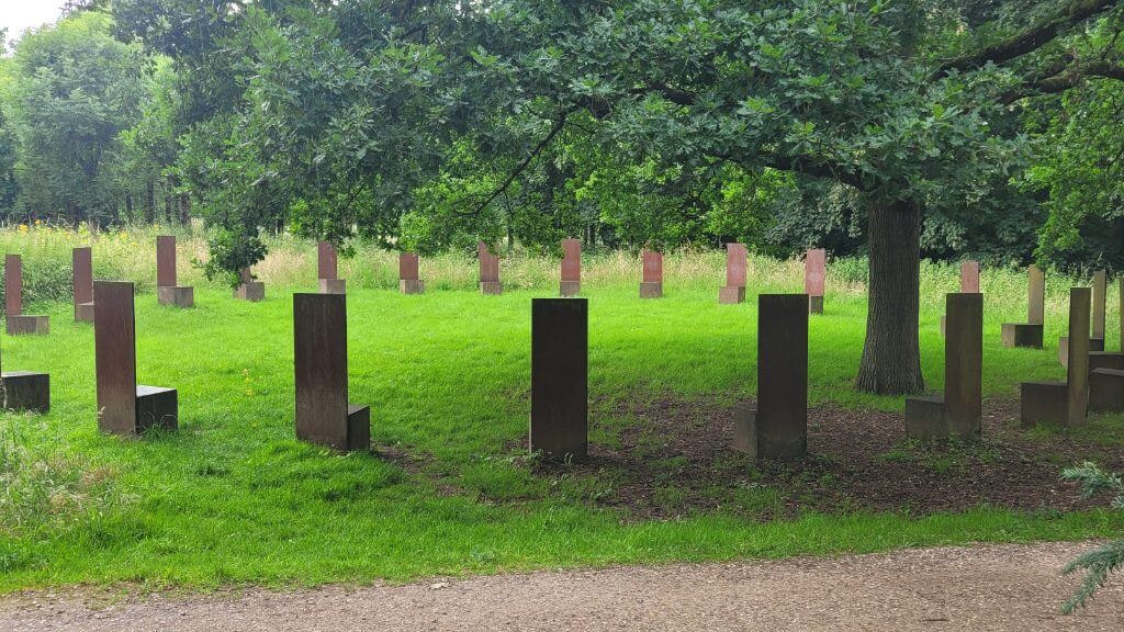 Ein Kreis aus rechteckigen Skulpturen auf einer Wiese unter Bäumen in einem Park.
