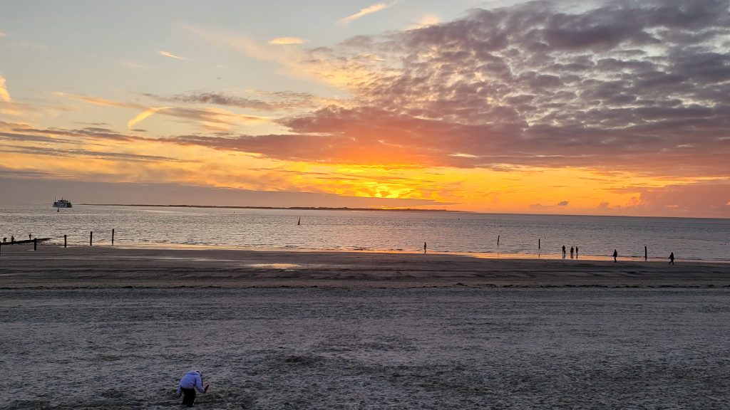 Blick auf einen bunten Sonnenuntergang mit ruhigem Meer und Strand im Vordergrund.