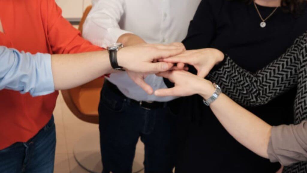 Mehrere Hände liegen übereinander als Symbol für Teamarbeit und Zusammenhalt.